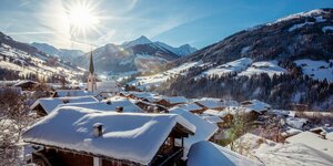 Alle Häuser voller Schnee, die Sonne scheint durch das Dorfzentrum von Alpbach, im Hintergrund die pure Winterlandschaft 